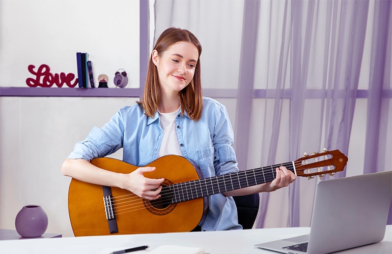 A woman watches a laptop screen while learning to play a C40 acoustic guitar.