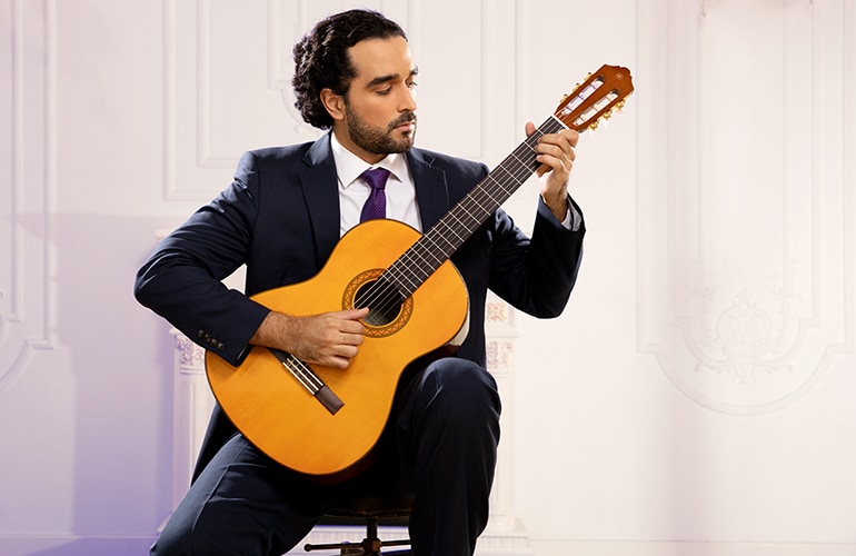 A well-dressed man plays the C70 acoustic guitar while seated.