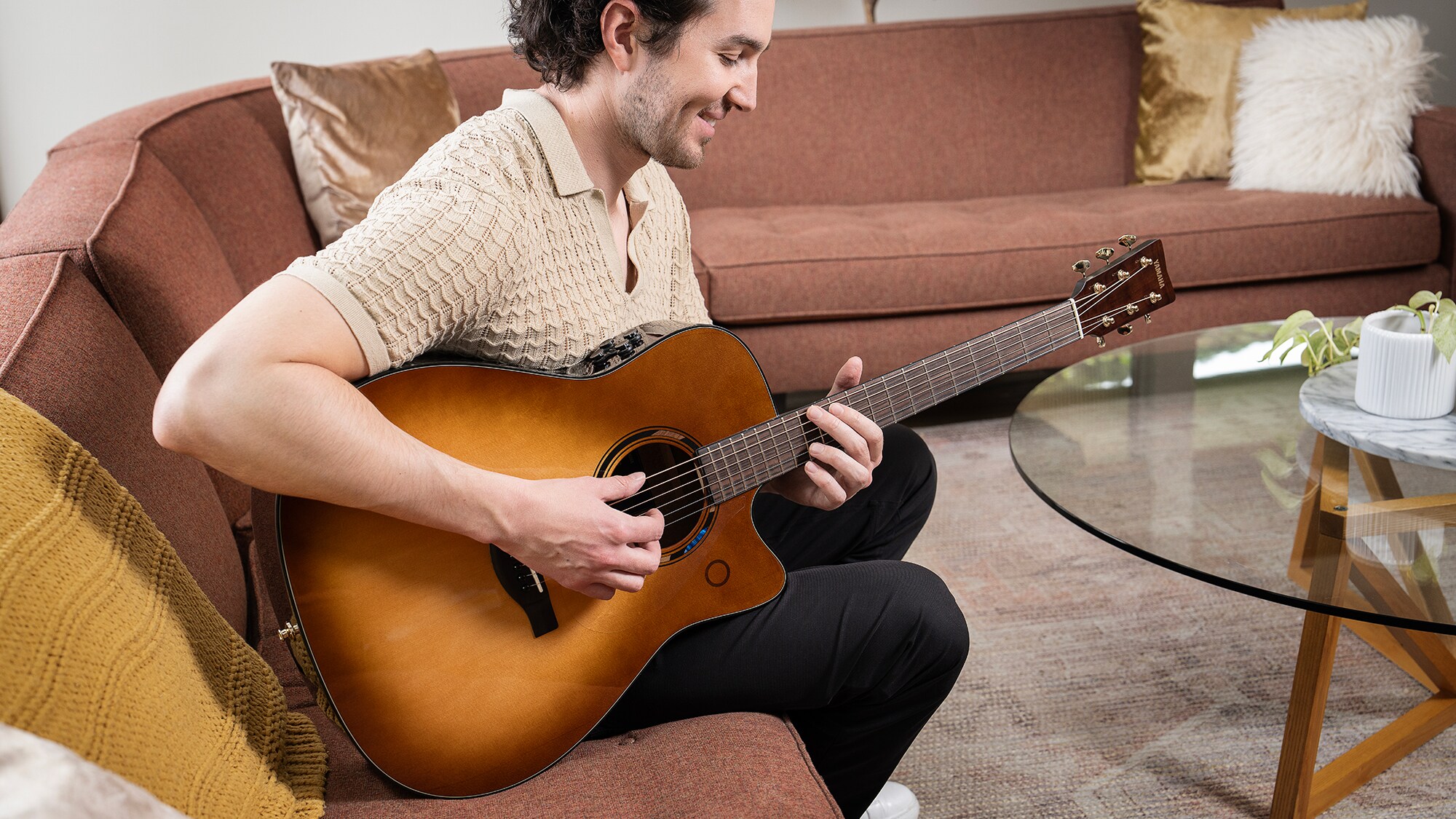 Ein Mann sitzt auf einem Sofa im Wohnzimmer und spielt eine TAG3 C Akustikgitarre