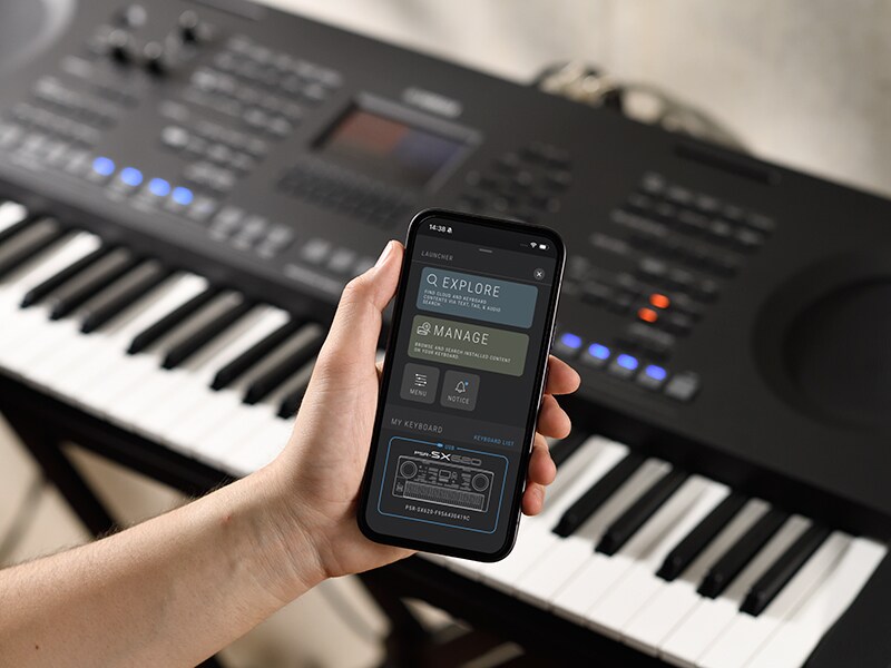 Das PSR-SX920 und eine Hand, die ein Smartphone mit der Anzeige eines Musik-Players hält.