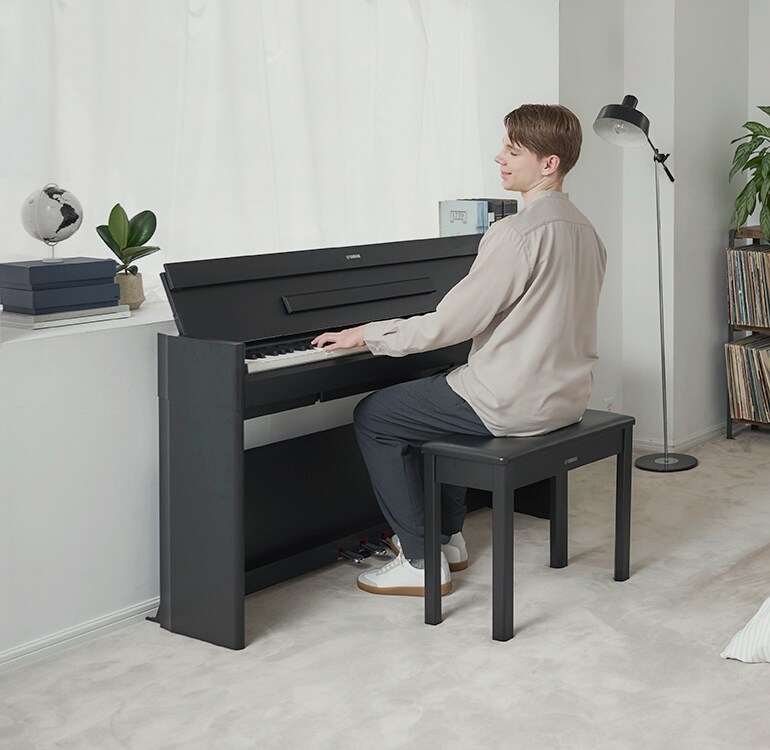 Ein Mann, der in entspannter Atmosphäre in einem Schlafzimmer auf einem ARIUS Piano spielt